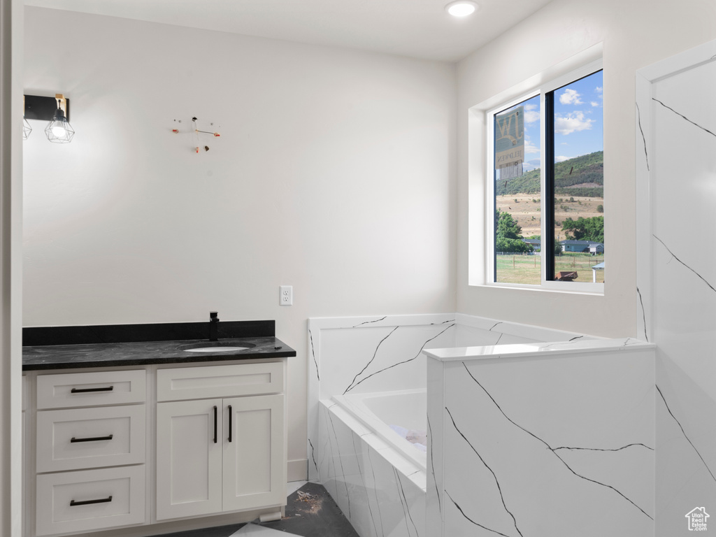 Bathroom featuring a relaxing tiled tub, vanity, and a healthy amount of sunlight