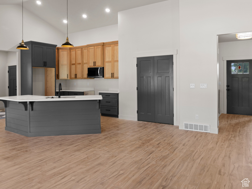 Kitchen with sink, high vaulted ceiling, light hardwood / wood-style flooring, and a center island with sink