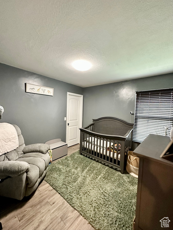 Bedroom with a textured ceiling, a nursery area, and wood-type flooring