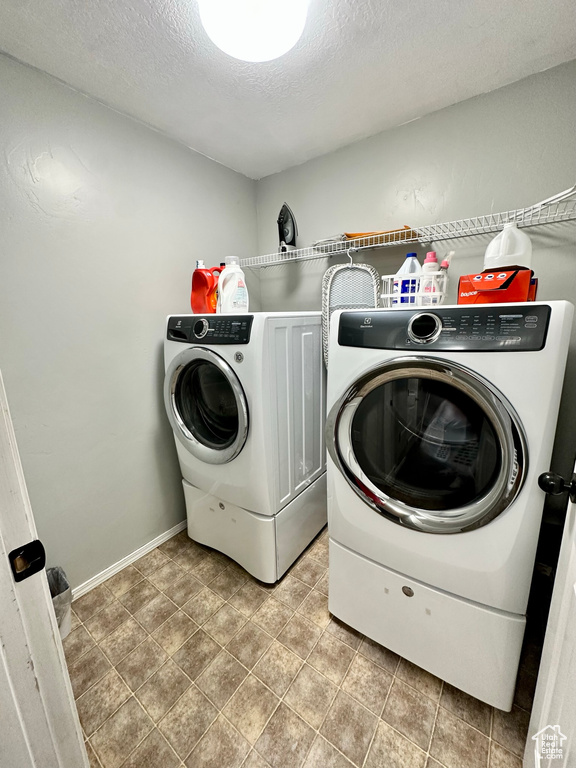 Laundry room featuring a textured ceiling, tile patterned floors, and washer and clothes dryer