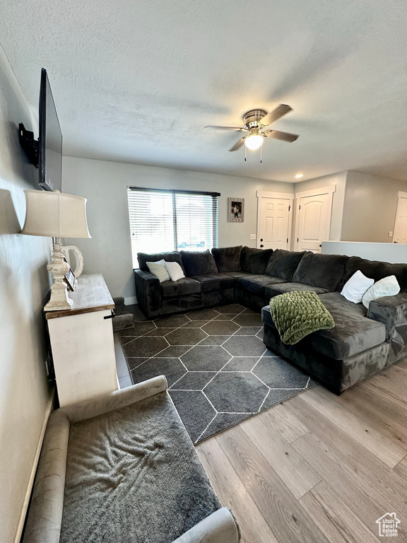 Living room with a textured ceiling, ceiling fan, and dark wood-type flooring