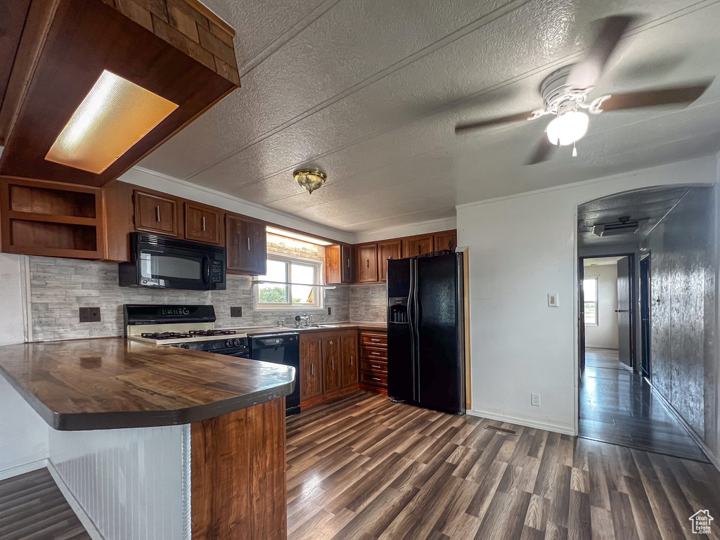 Kitchen featuring black appliances, kitchen peninsula, backsplash, dark wood-type flooring, and ceiling fan