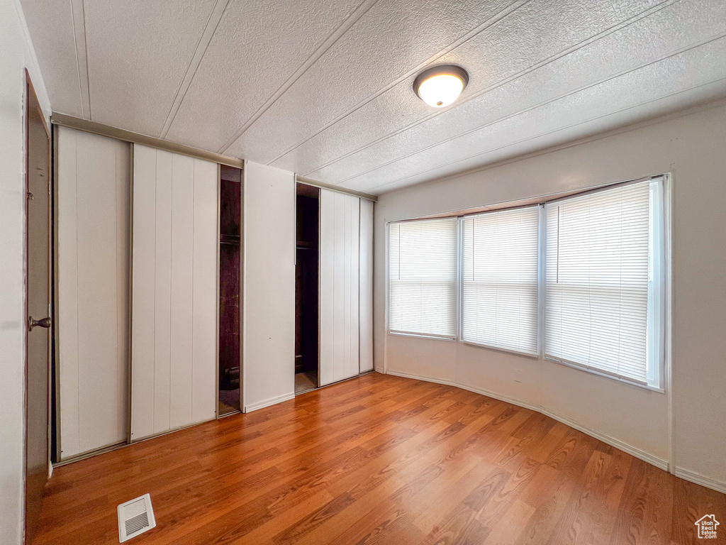 Unfurnished bedroom with multiple closets, light wood-type flooring, and a textured ceiling