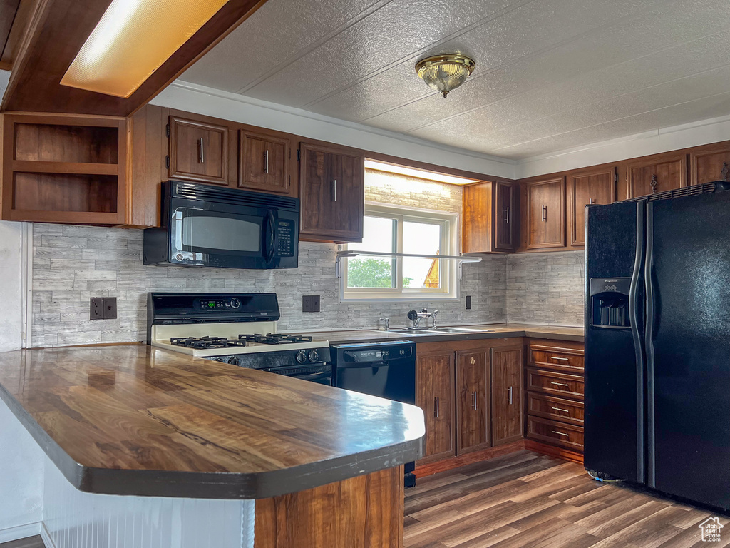 Kitchen featuring black appliances, dark hardwood / wood-style flooring, wood counters, kitchen peninsula, and backsplash