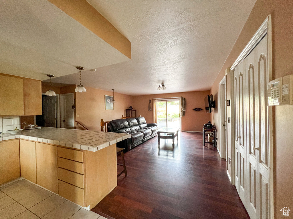 Kitchen with tile counters, kitchen peninsula, dark hardwood / wood-style flooring, hanging light fixtures, and a kitchen bar