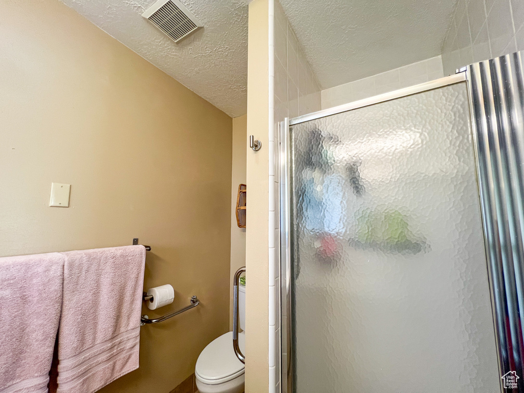 Bathroom featuring toilet, a textured ceiling, and walk in shower