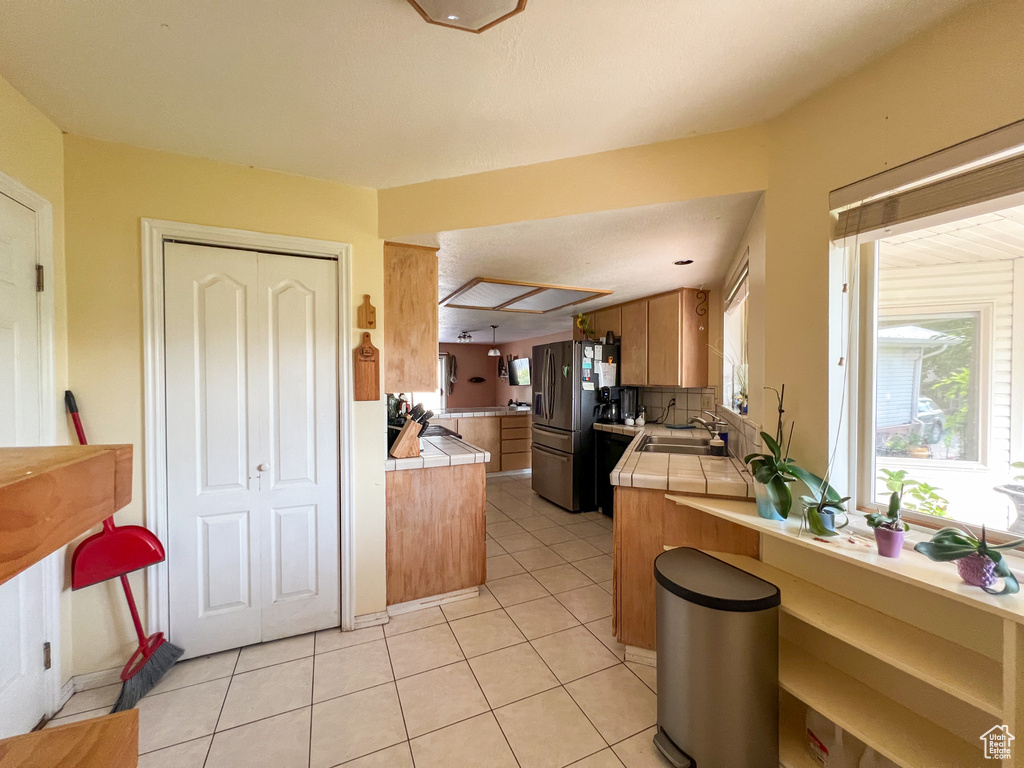 Kitchen with stainless steel fridge, sink, kitchen peninsula, decorative backsplash, and tile countertops