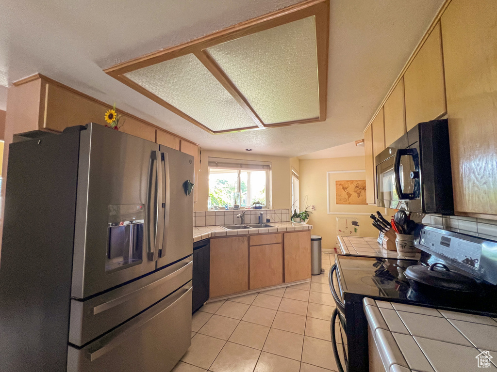 Kitchen featuring appliances with stainless steel finishes, tile counters, backsplash, and light tile patterned floors