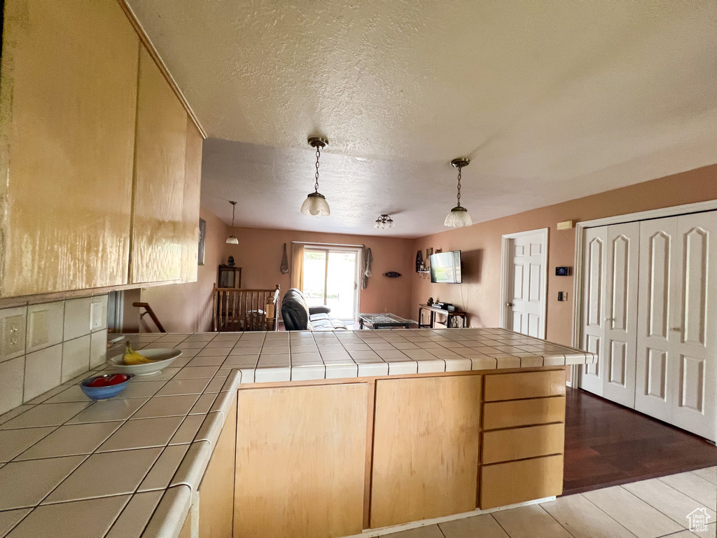 Kitchen with light brown cabinets, kitchen peninsula, decorative light fixtures, tile countertops, and dark hardwood / wood-style flooring