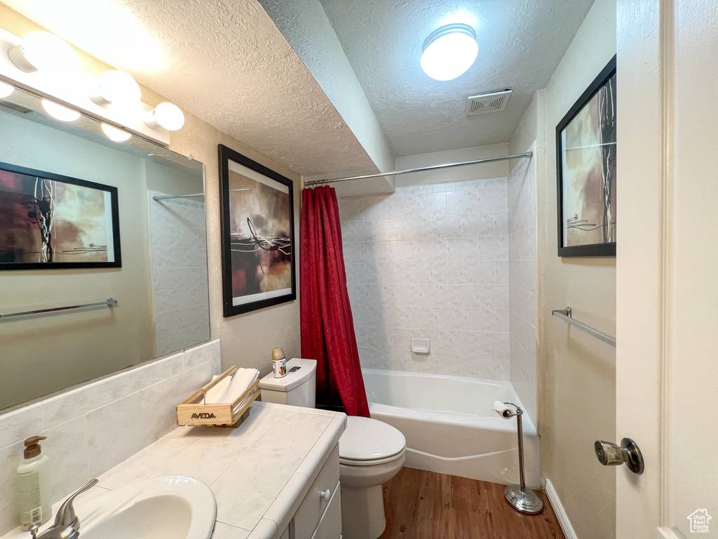 Full bathroom with vanity, hardwood / wood-style flooring, shower / bath combination with curtain, toilet, and a textured ceiling