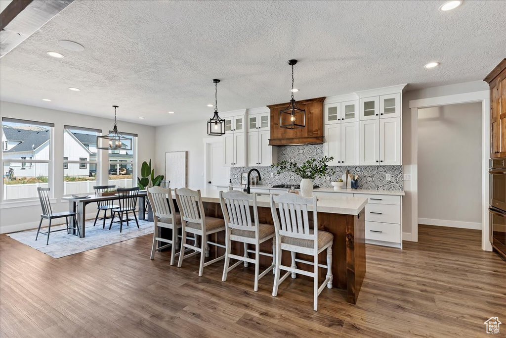 Kitchen with hanging light fixtures, white cabinets, dark hardwood / wood-style floors, and a kitchen island with sink