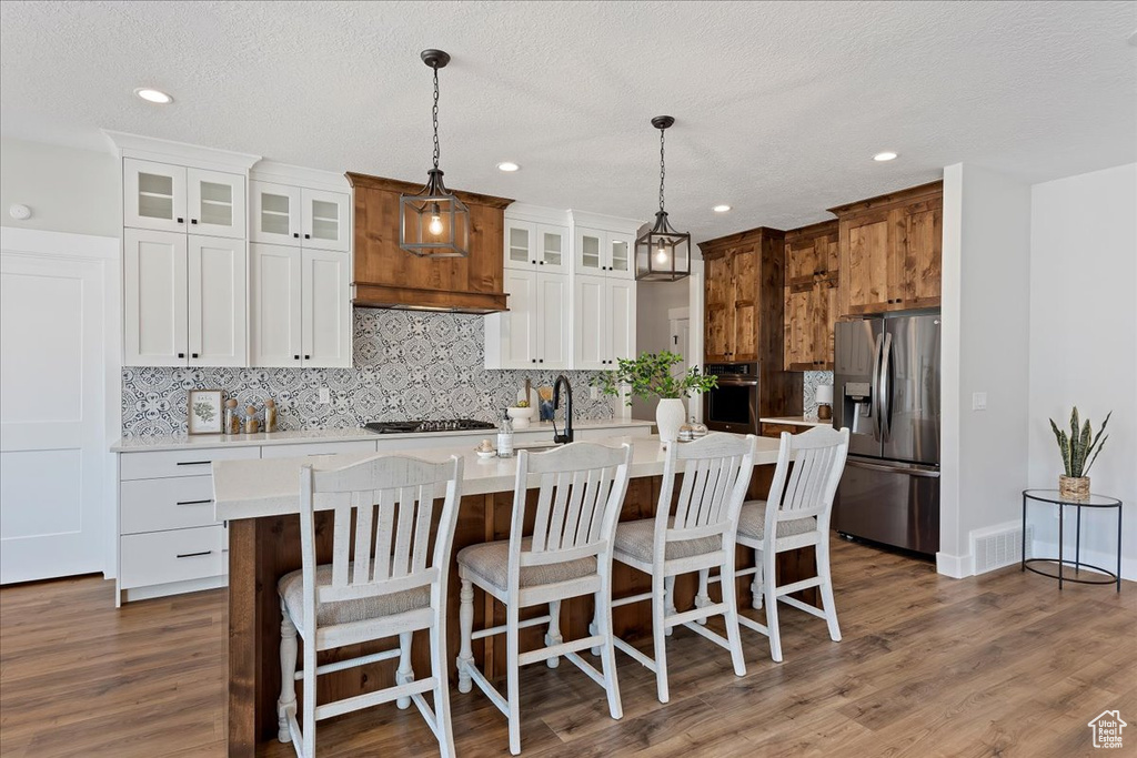 Kitchen with appliances with stainless steel finishes, dark hardwood / wood-style flooring, a center island with sink, and white cabinetry