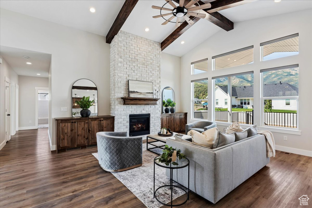 Living room with beam ceiling, dark hardwood / wood-style floors, a brick fireplace, and ceiling fan