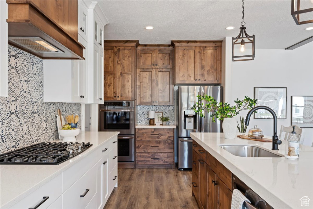 Kitchen featuring stainless steel appliances, sink, custom exhaust hood, white cabinetry, and dark wood-type flooring