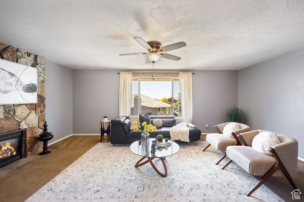 Living room featuring a textured ceiling, a fireplace, carpet floors, and ceiling fan