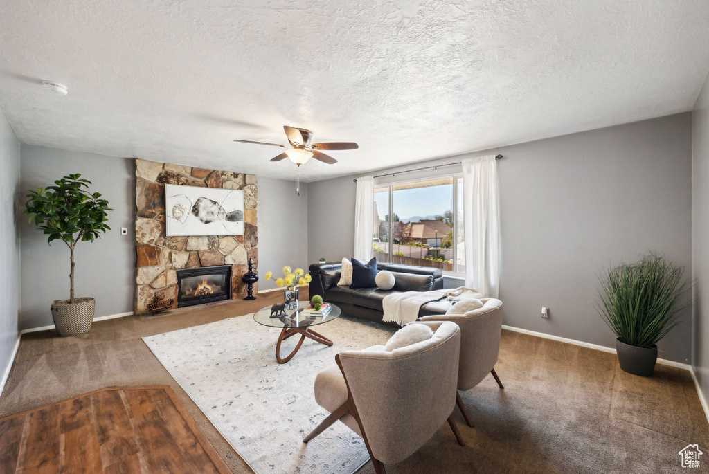 Carpeted living room with a textured ceiling, ceiling fan, and a fireplace