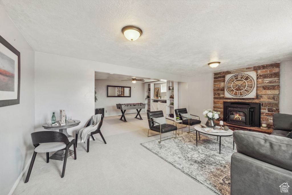 Living room featuring ceiling fan, a fireplace, carpet flooring, a textured ceiling, and brick wall