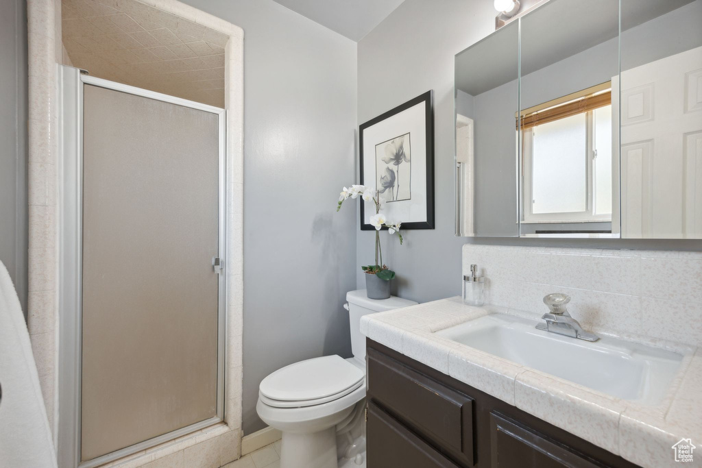 Bathroom with tile flooring, tasteful backsplash, a shower with door, toilet, and vanity