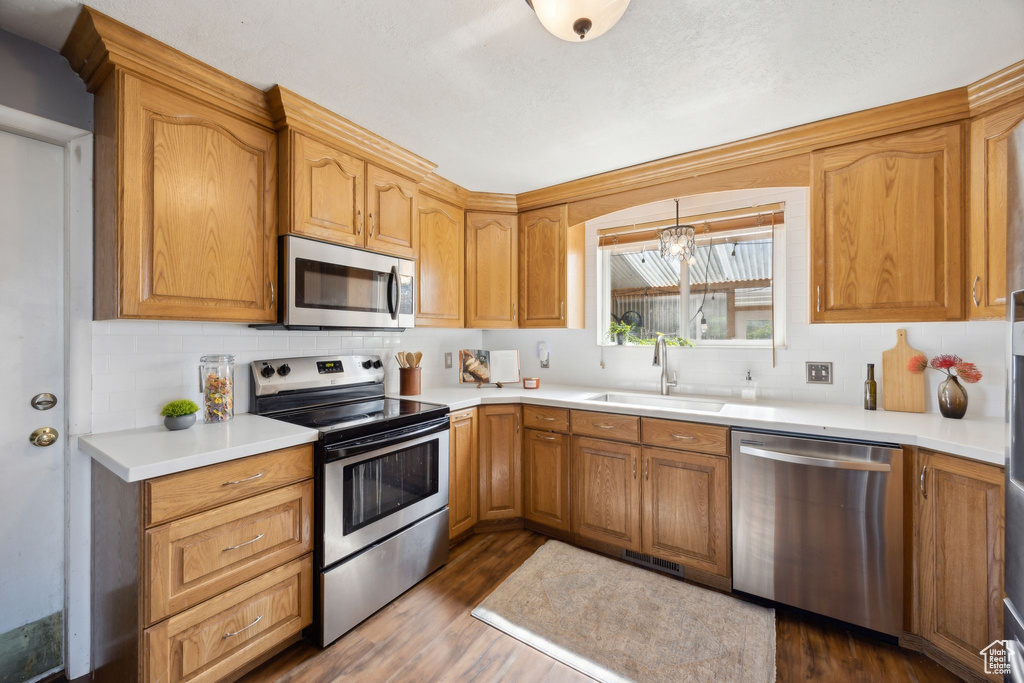 Kitchen featuring dark hardwood / wood-style flooring, appliances with stainless steel finishes, pendant lighting, a notable chandelier, and sink