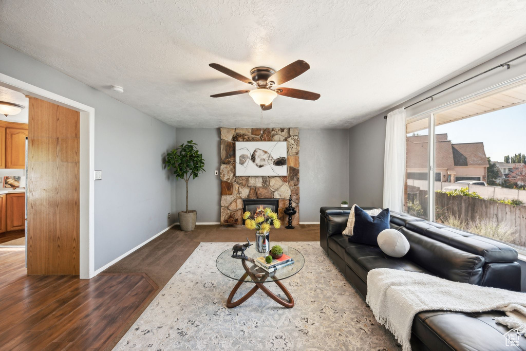 Living room featuring a stone fireplace, a textured ceiling, wood-type flooring, and ceiling fan