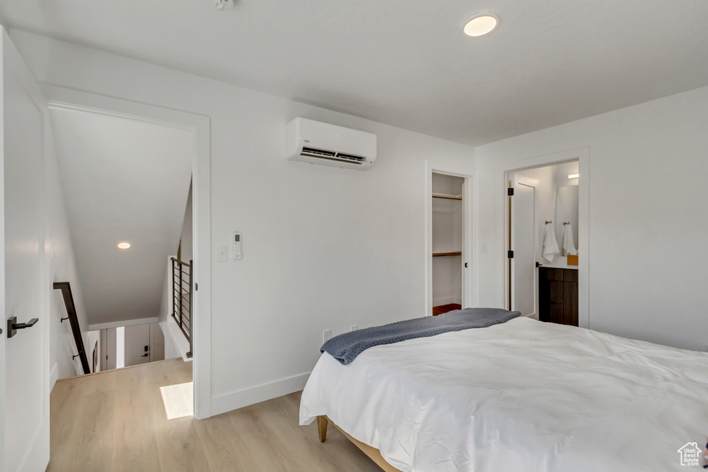 Bedroom with an AC wall unit, light wood-type flooring, connected bathroom, a spacious closet, and a closet