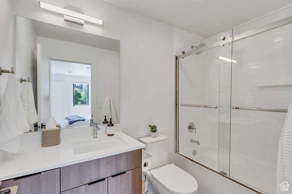 Full bathroom with bath / shower combo with glass door, vanity, and toilet