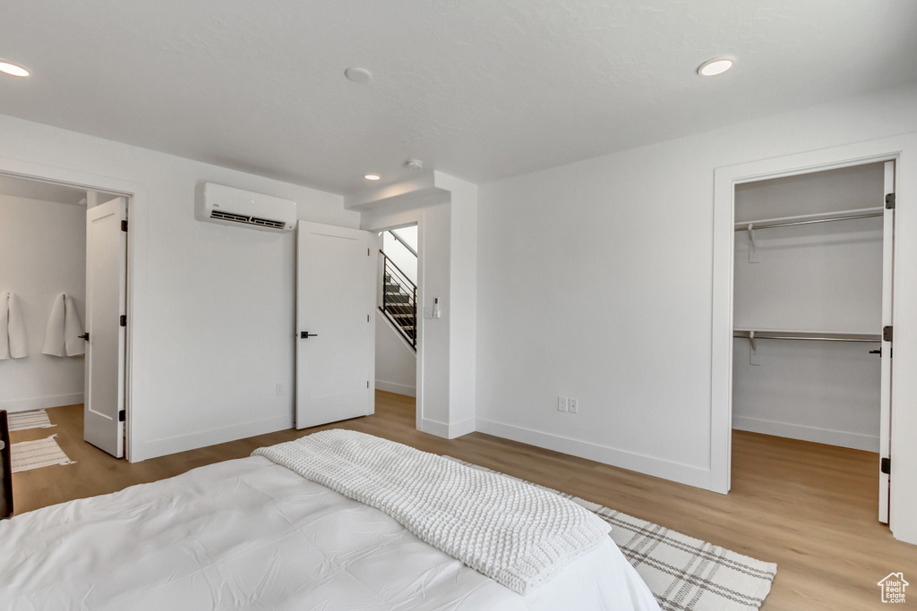 Bedroom with a wall mounted air conditioner, a spacious closet, light hardwood / wood-style flooring, and a closet