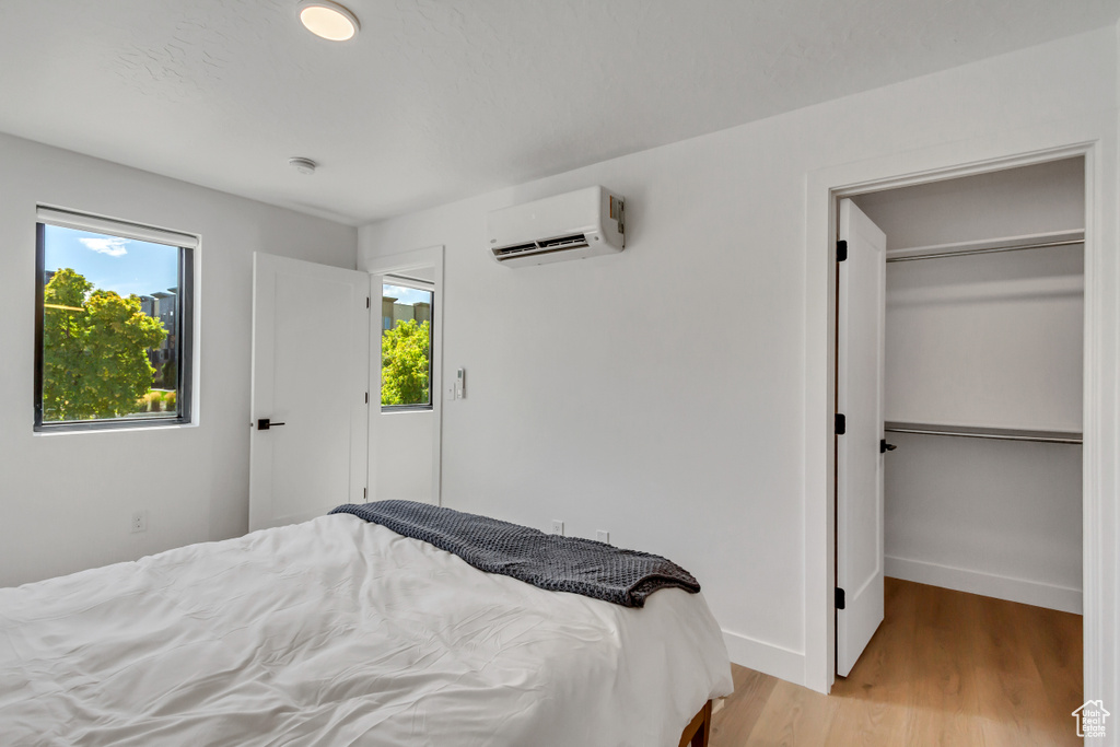 Bedroom featuring a wall mounted AC, multiple windows, and light hardwood / wood-style flooring