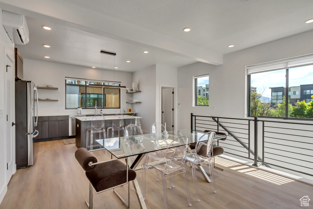 Dining area featuring sink, a wall mounted AC, light hardwood / wood-style flooring, and beam ceiling