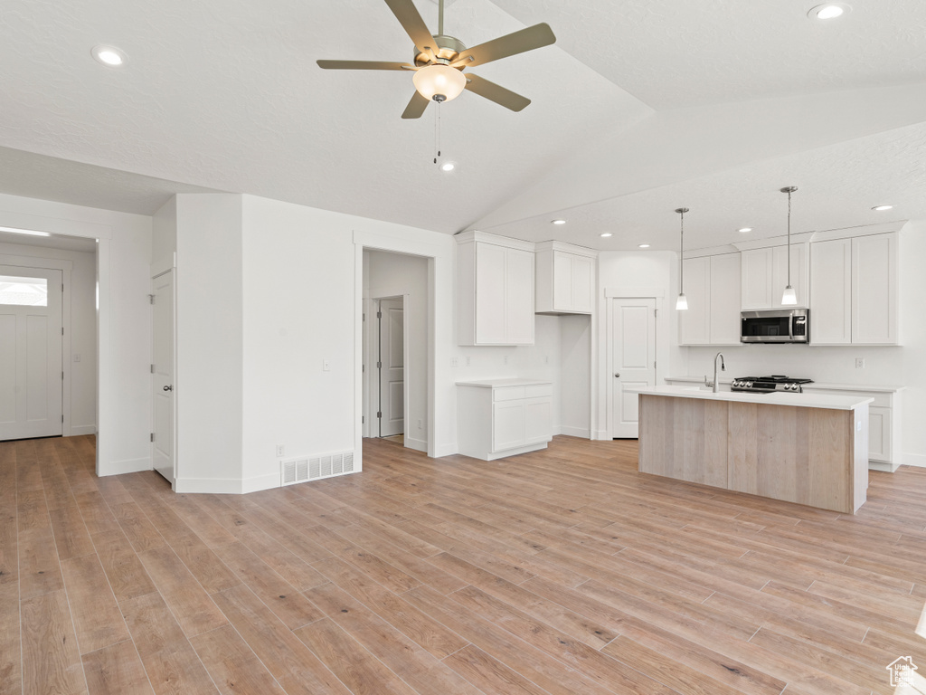 Kitchen with light hardwood / wood-style flooring, stainless steel appliances, white cabinetry, ceiling fan, and a center island with sink