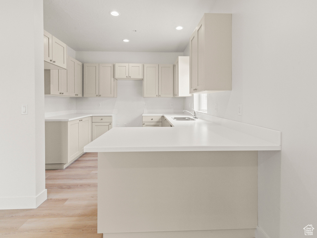 Kitchen with sink, light hardwood / wood-style flooring, white cabinetry, and kitchen peninsula