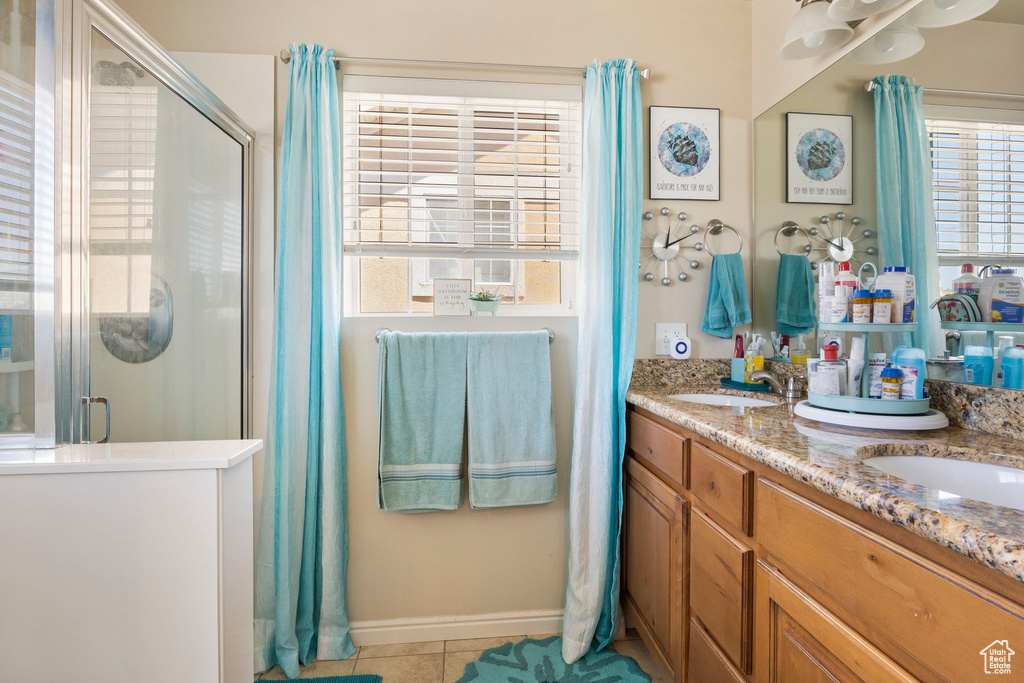 Bathroom featuring a shower with shower door, tile patterned floors, a wealth of natural light, and dual bowl vanity