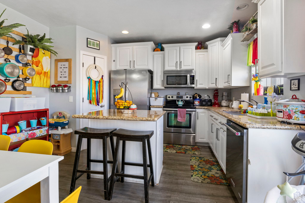 Kitchen with white cabinetry, a center island, dark hardwood / wood-style flooring, and appliances with stainless steel finishes