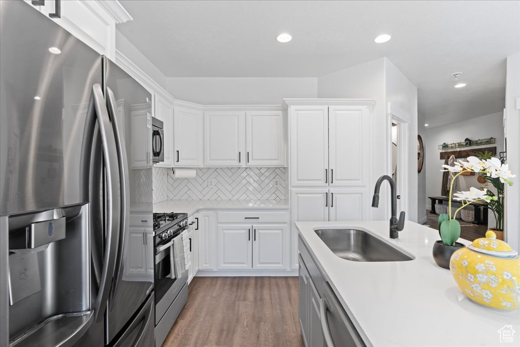 Kitchen featuring appliances with stainless steel finishes, hardwood / wood-style floors, sink, backsplash, and white cabinetry