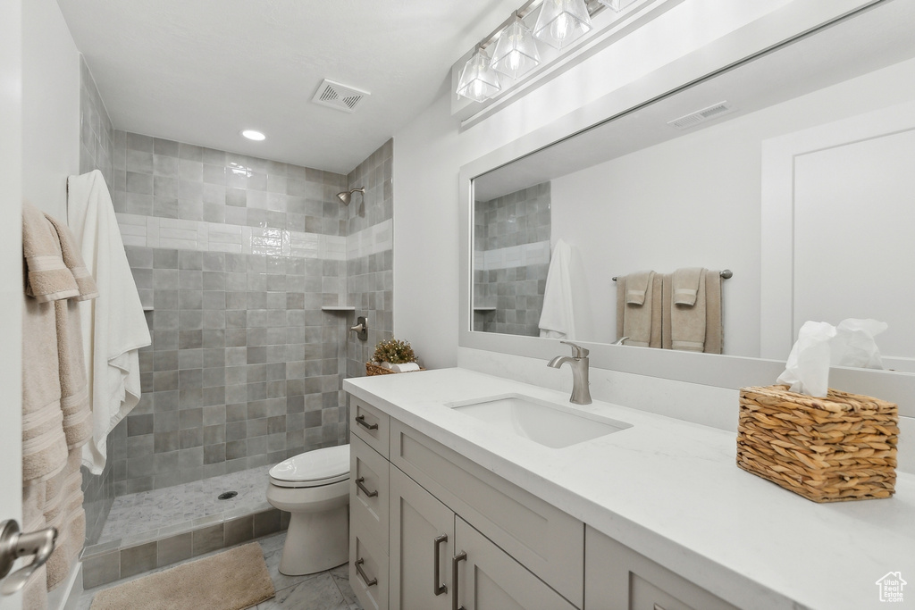 Bathroom featuring vanity, tile patterned flooring, a tile shower, and toilet