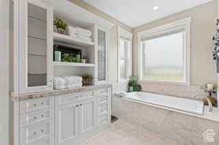 Bathroom featuring a relaxing tiled tub, vanity, and tile patterned flooring