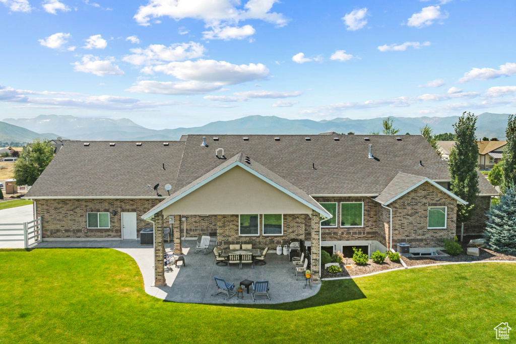 Back of property featuring a mountain view, a patio area, central air condition unit, and a yard