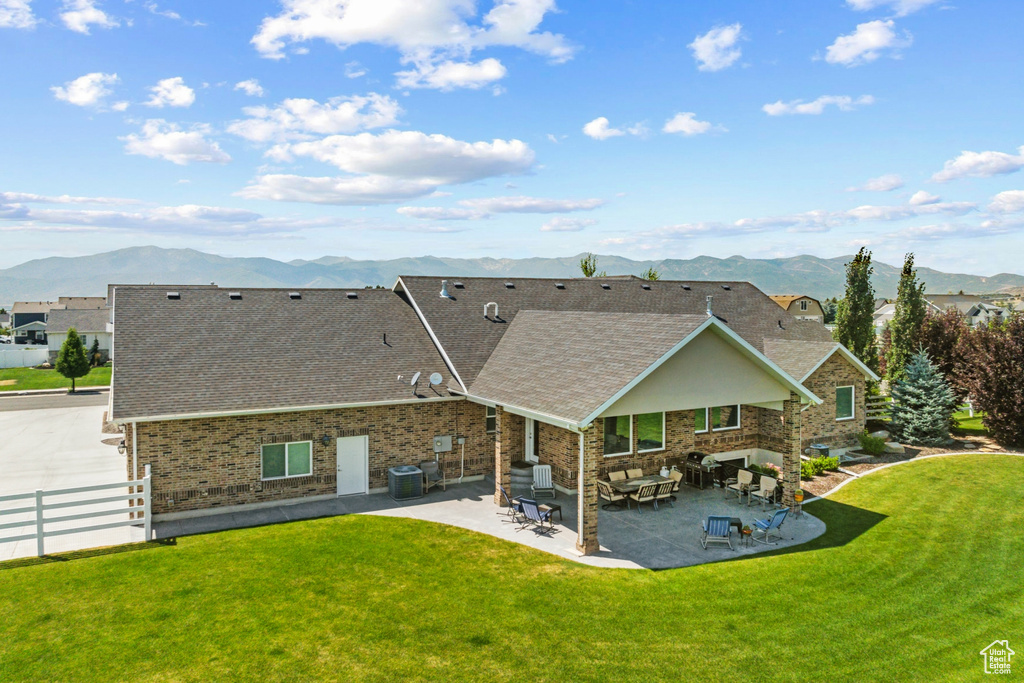 Back of property with cooling unit, a mountain view, a lawn, and a patio area