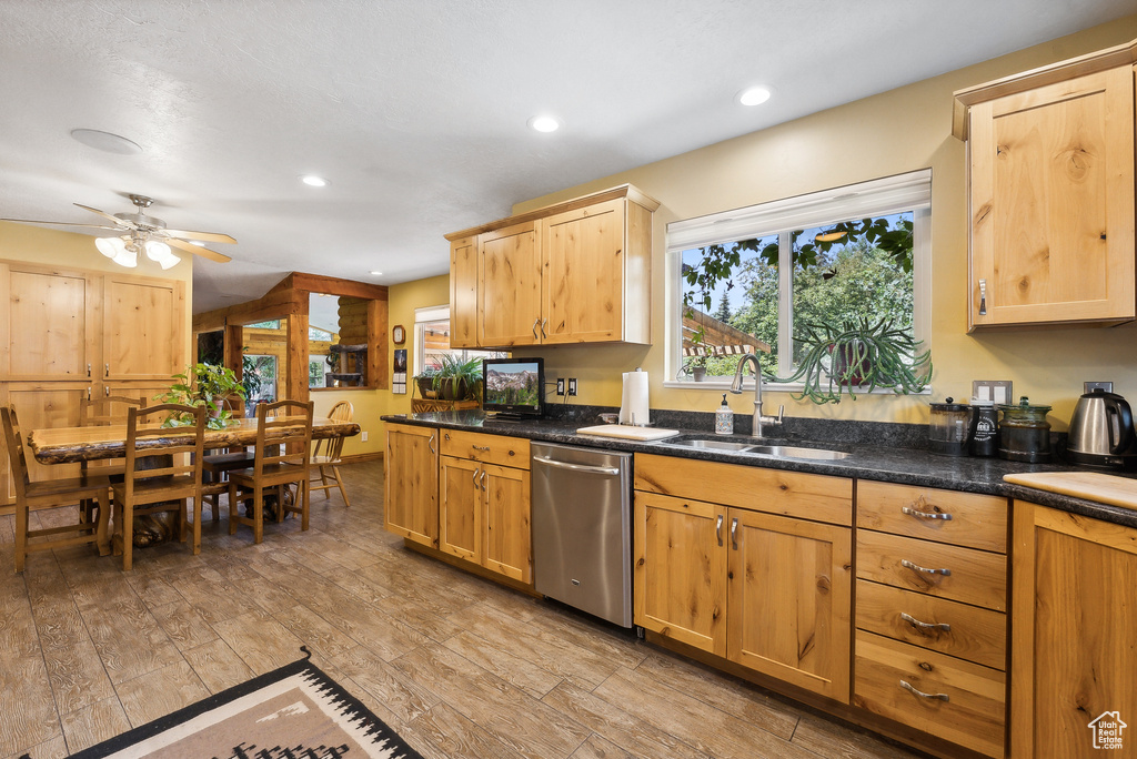 Kitchen featuring light hardwood / wood-style flooring, dark stone counters, sink, stainless steel dishwasher, and ceiling fan