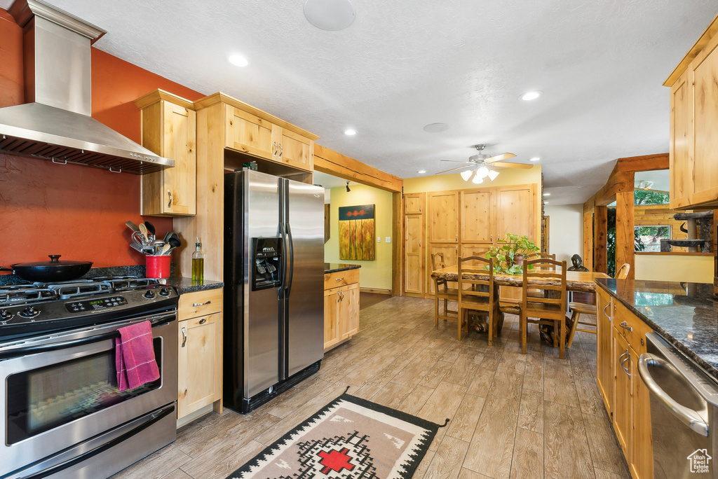 Kitchen with light hardwood / wood-style flooring, ceiling fan, stainless steel appliances, wall chimney exhaust hood, and light brown cabinetry