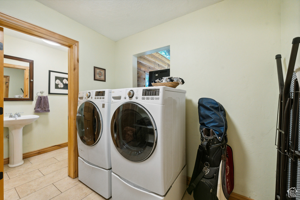 Clothes washing area featuring sink, light tile patterned flooring, and washing machine and dryer