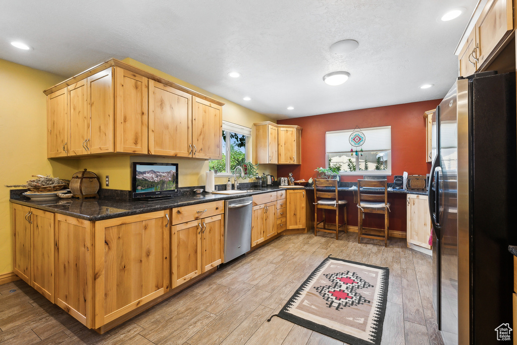 Kitchen featuring dark stone counters, stainless steel dishwasher, black refrigerator, light wood-type flooring, and kitchen peninsula