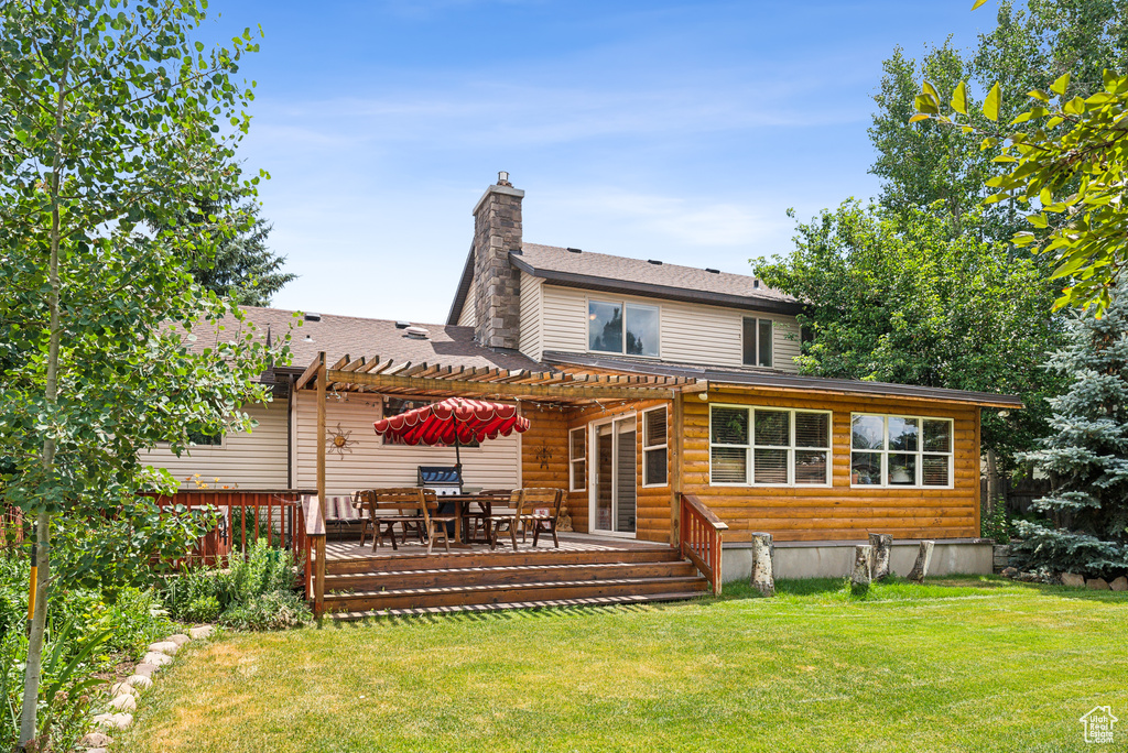 Back of property with a wooden deck, a yard, and a pergola