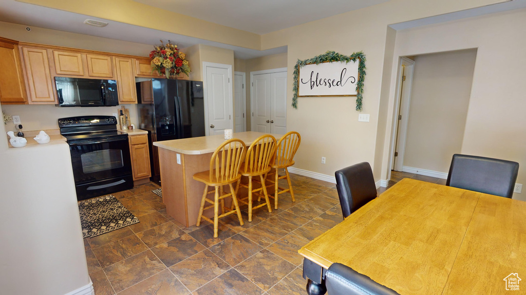 Kitchen with black appliances, dark tile patterned floors, light brown cabinets, a center island, and a kitchen breakfast bar