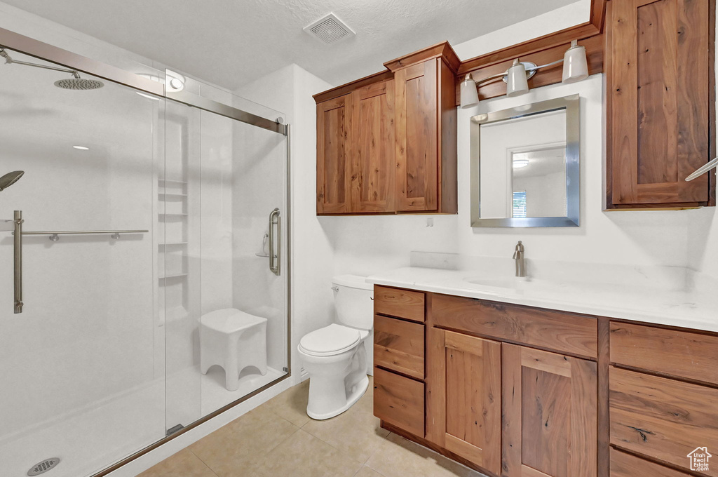 Bathroom with vanity, an enclosed shower, toilet, a textured ceiling, and tile patterned flooring