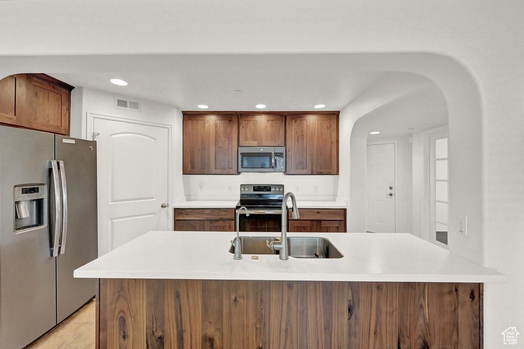 Kitchen with light tile patterned flooring, sink, stainless steel appliances, and a center island with sink