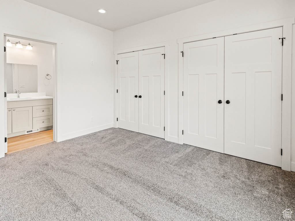 Unfurnished bedroom featuring multiple closets, carpet, sink, and ensuite bath