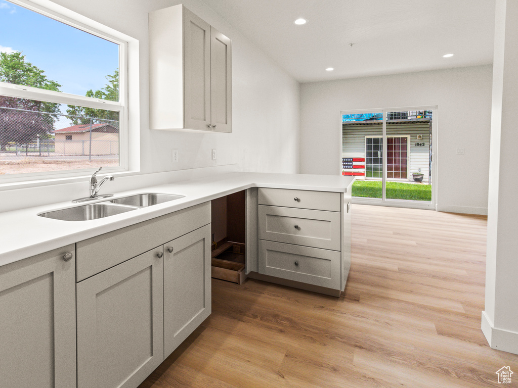 Kitchen with gray cabinetry, light hardwood / wood-style flooring, sink, and kitchen peninsula