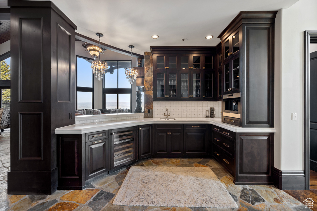 Bar featuring a notable chandelier, beverage cooler, decorative backsplash, pendant lighting, and oven