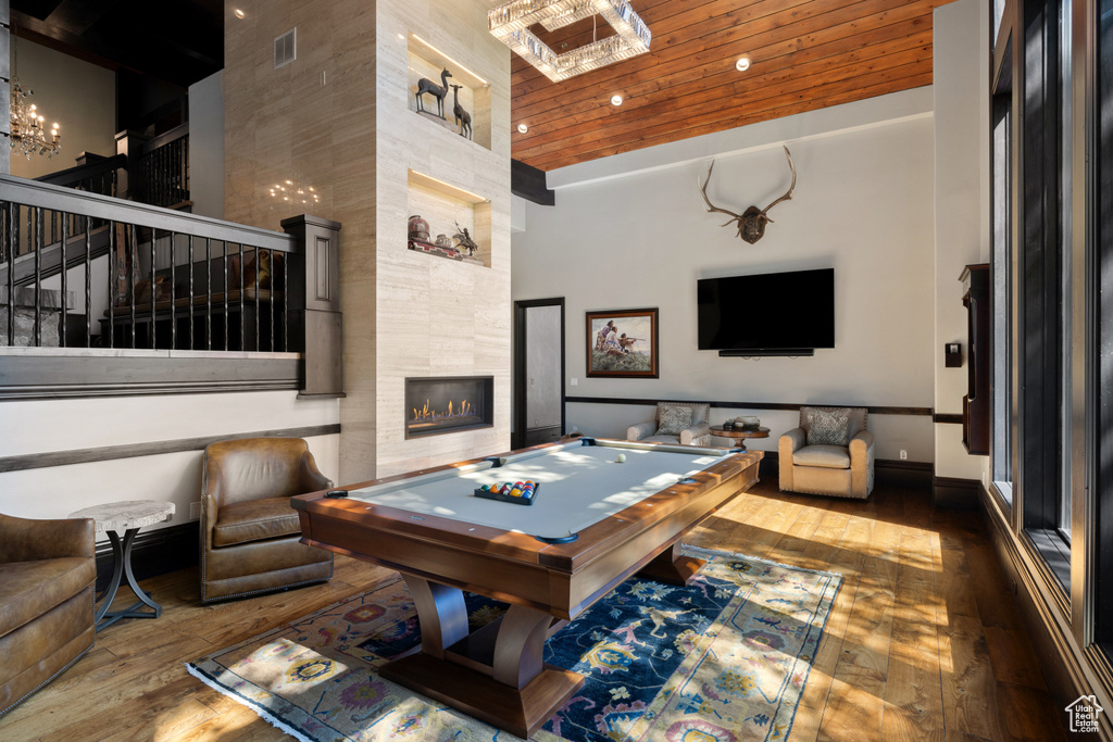 Playroom featuring a notable chandelier, pool table, dark hardwood / wood-style flooring, a towering ceiling, and a tiled fireplace